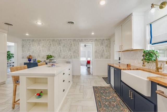 kitchen with white cabinets, a breakfast bar, dishwasher, butcher block counters, and sink