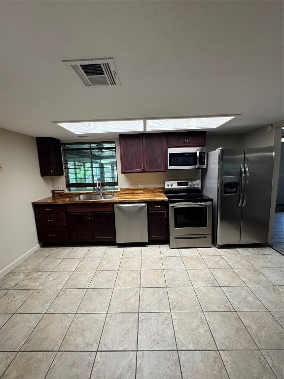 kitchen featuring stainless steel appliances, wood counters, sink, and light tile patterned flooring