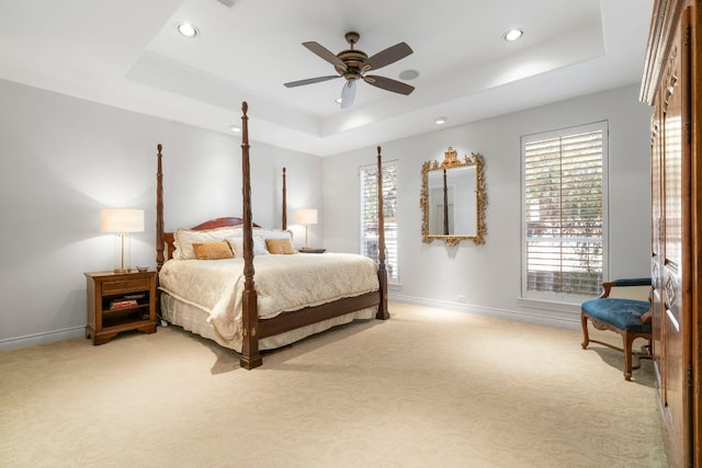 bedroom with a tray ceiling, light carpet, and multiple windows