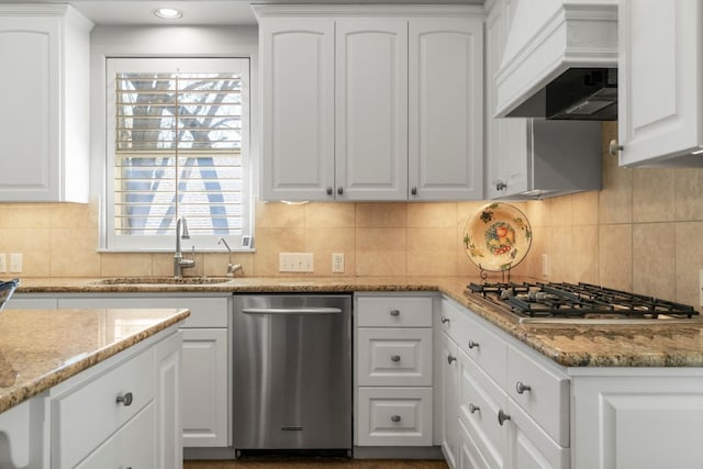 kitchen with a sink, range hood, stainless steel appliances, white cabinetry, and backsplash