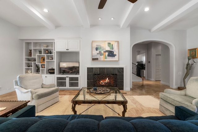 living area with arched walkways, recessed lighting, a tile fireplace, beamed ceiling, and baseboards