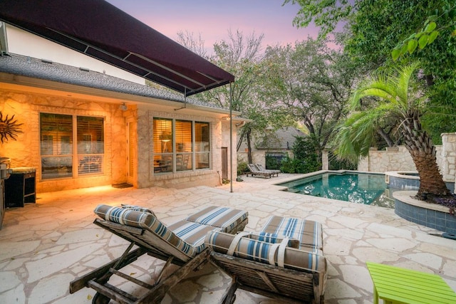 pool at dusk featuring a patio, an outdoor pool, and an in ground hot tub