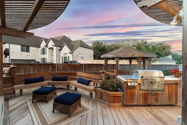 deck at dusk featuring exterior kitchen, a gazebo, area for grilling, and a pergola