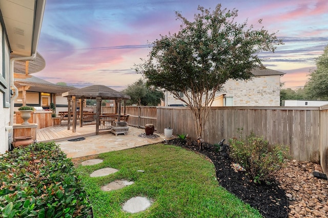 yard at dusk featuring a wooden deck, a gazebo, and a patio