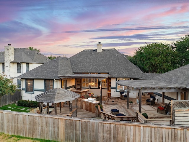 back house at dusk with a wooden deck and a pergola