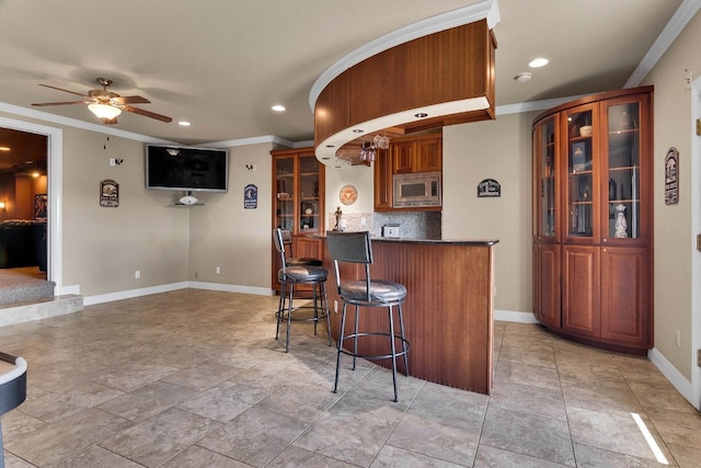 kitchen featuring stainless steel microwave, a kitchen breakfast bar, ceiling fan, crown molding, and decorative backsplash