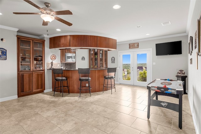 kitchen with kitchen peninsula, stainless steel microwave, a kitchen bar, ornamental molding, and french doors