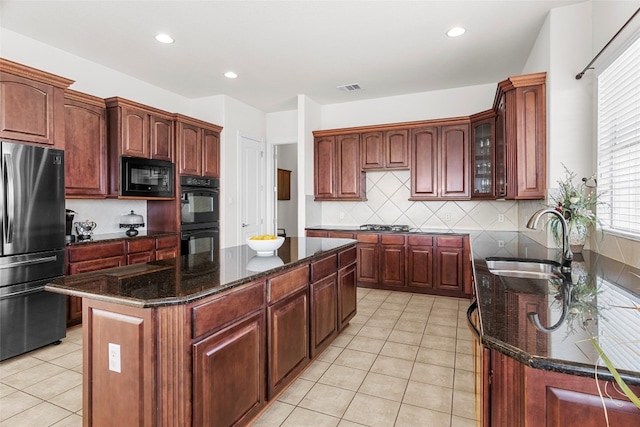 kitchen featuring tasteful backsplash, dark stone counters, black appliances, sink, and a center island