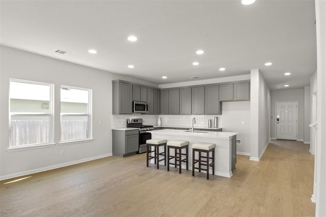 kitchen with stainless steel appliances, a breakfast bar area, a center island with sink, and gray cabinets