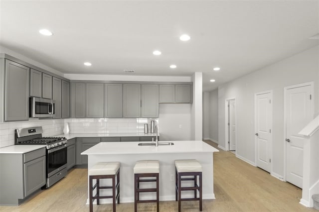 kitchen with a kitchen island with sink, a kitchen breakfast bar, gray cabinetry, stainless steel appliances, and light wood-type flooring