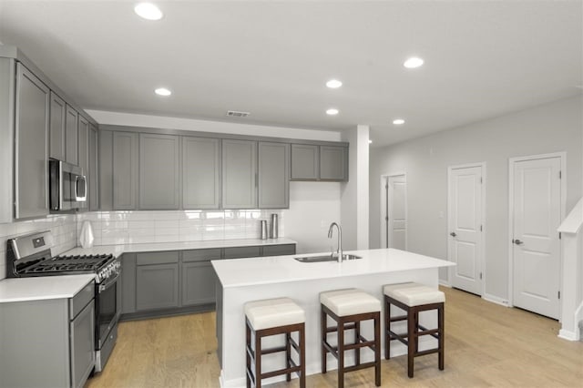 kitchen with gray cabinetry, stainless steel appliances, sink, and a center island with sink