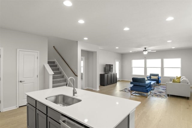 kitchen featuring a kitchen island with sink, sink, light wood-type flooring, stainless steel dishwasher, and ceiling fan