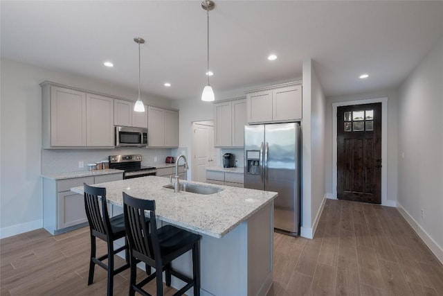 kitchen featuring wood finished floors, a sink, baseboards, stainless steel appliances, and an island with sink