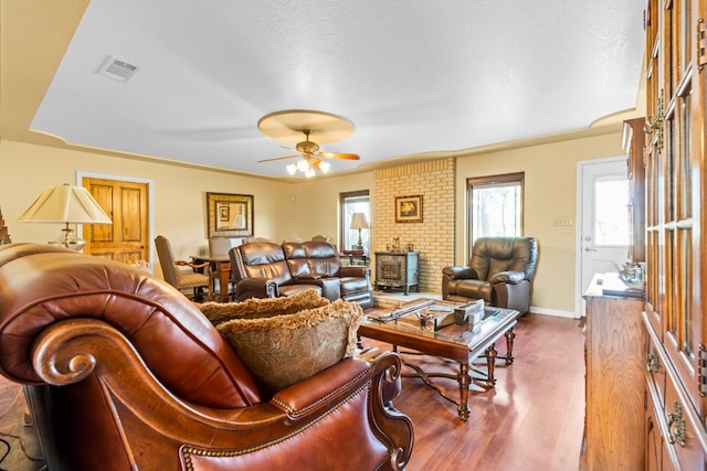 living room featuring ceiling fan, a wood stove, a textured ceiling, and hardwood / wood-style floors