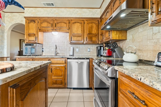 kitchen featuring decorative backsplash, light tile patterned floors, light stone countertops, range hood, and stainless steel appliances