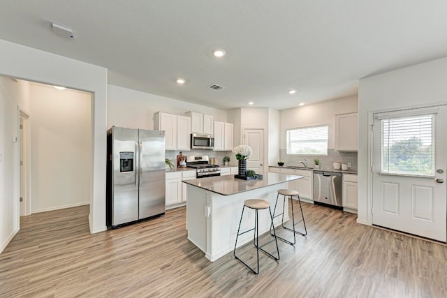 kitchen with white cabinetry, a center island, stainless steel appliances, light hardwood / wood-style floors, and a breakfast bar