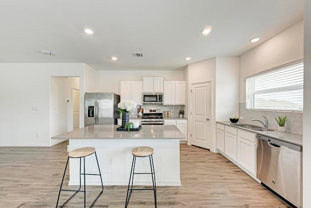 kitchen featuring light wood-type flooring, stainless steel appliances, sink, a center island, and white cabinetry