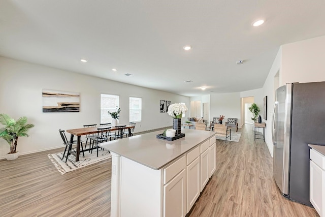 kitchen with white cabinets, a center island, light hardwood / wood-style flooring, and stainless steel refrigerator