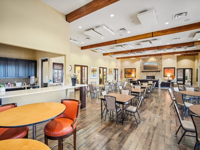 dining space featuring beam ceiling, a stone fireplace, and hardwood / wood-style floors