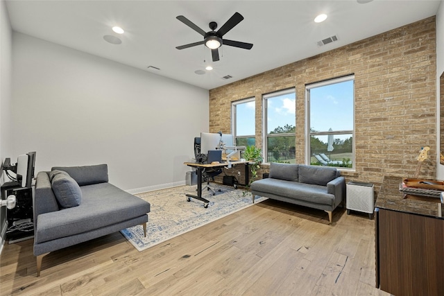 interior space with ceiling fan, brick wall, and light wood-type flooring