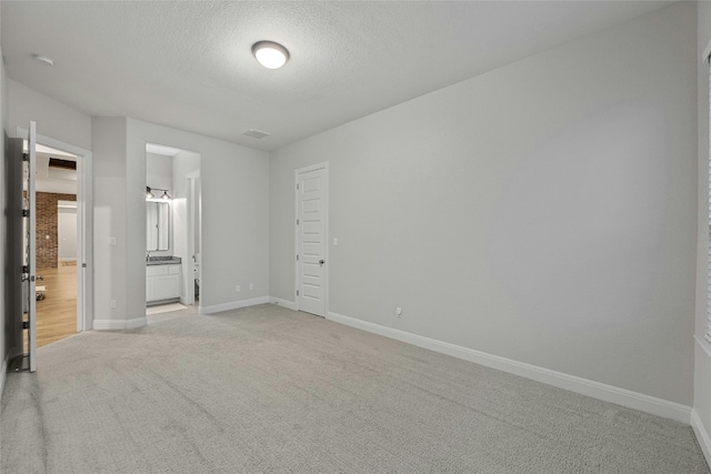 unfurnished bedroom featuring connected bathroom, a textured ceiling, and light colored carpet