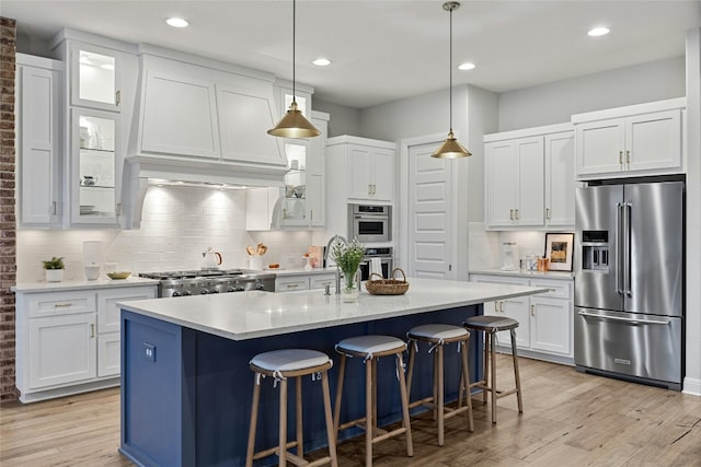 kitchen with stainless steel appliances, hanging light fixtures, light wood-type flooring, and white cabinets