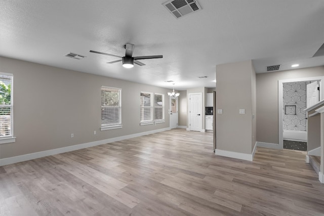 unfurnished living room with a textured ceiling, light hardwood / wood-style floors, ceiling fan with notable chandelier, and a healthy amount of sunlight