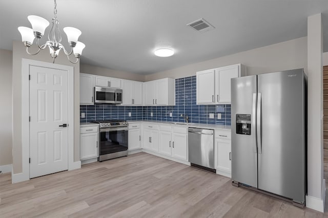 kitchen with an inviting chandelier, appliances with stainless steel finishes, white cabinets, and light hardwood / wood-style floors