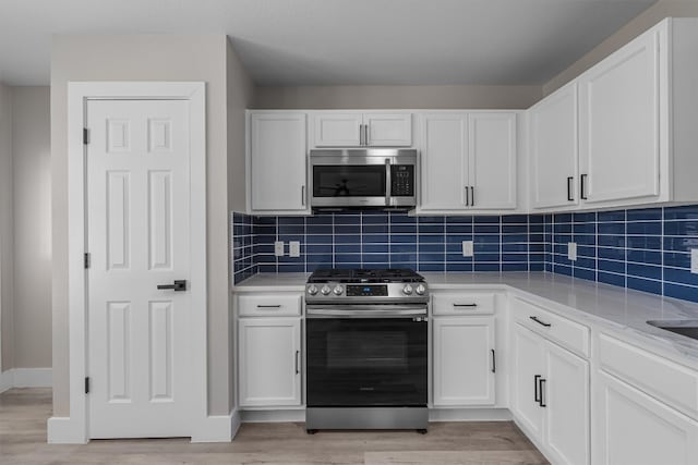 kitchen featuring backsplash, white cabinetry, stainless steel appliances, and light hardwood / wood-style floors