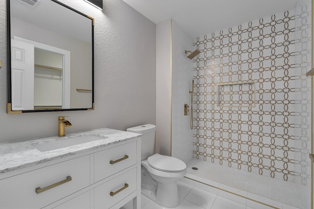 bathroom featuring a tile shower, vanity, toilet, and tile patterned flooring