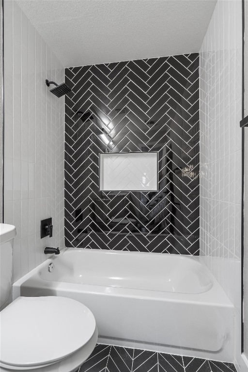 bathroom featuring toilet, a textured ceiling, and tiled shower / bath