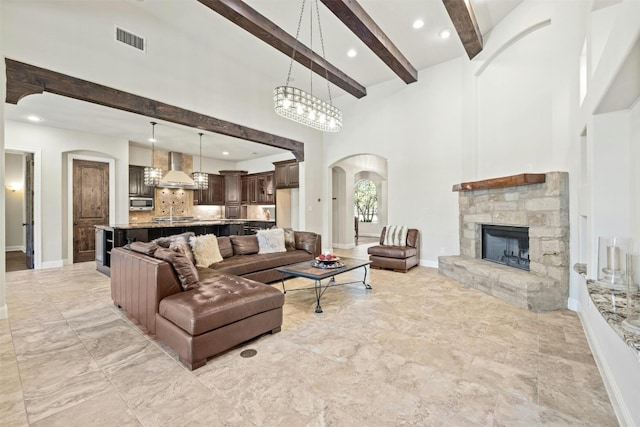 living room featuring arched walkways, a stone fireplace, visible vents, baseboards, and beamed ceiling