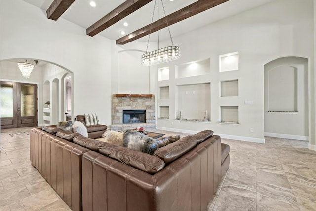 living room featuring baseboards, arched walkways, a high ceiling, a stone fireplace, and beam ceiling