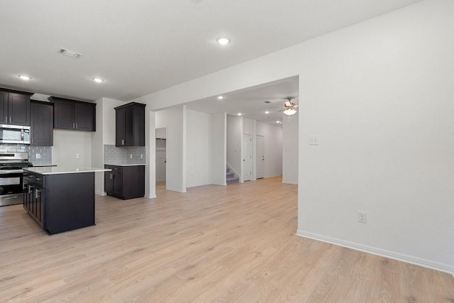 kitchen with ceiling fan, a center island, light hardwood / wood-style flooring, backsplash, and appliances with stainless steel finishes