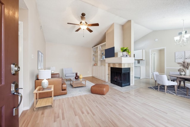 living room with light wood-type flooring, ceiling fan with notable chandelier, built in features, lofted ceiling, and a tiled fireplace