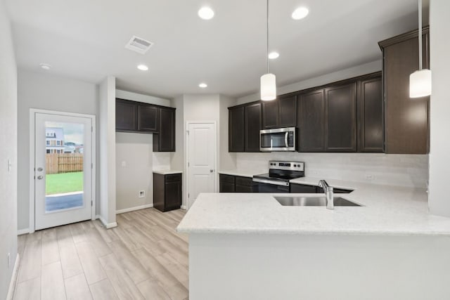 kitchen with kitchen peninsula, appliances with stainless steel finishes, light hardwood / wood-style flooring, sink, and decorative light fixtures