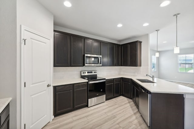 kitchen featuring kitchen peninsula, sink, pendant lighting, light hardwood / wood-style floors, and stainless steel appliances