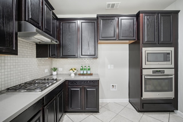 kitchen with appliances with stainless steel finishes, dark brown cabinetry, backsplash, and light tile patterned floors