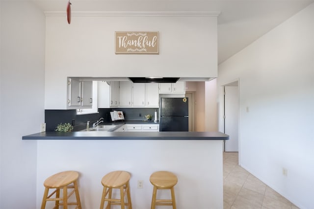 kitchen featuring decorative backsplash, black fridge, kitchen peninsula, sink, and crown molding