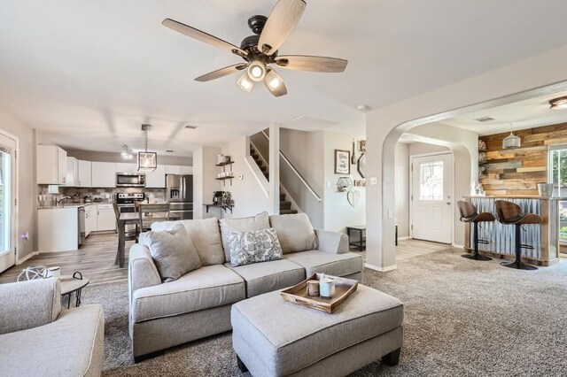 living room with wooden walls, ceiling fan, and light hardwood / wood-style floors