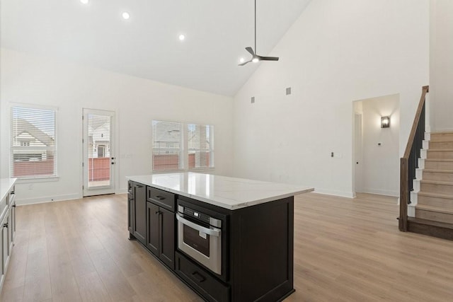 kitchen featuring light stone counters, stainless steel oven, high vaulted ceiling, a kitchen island, and light hardwood / wood-style floors