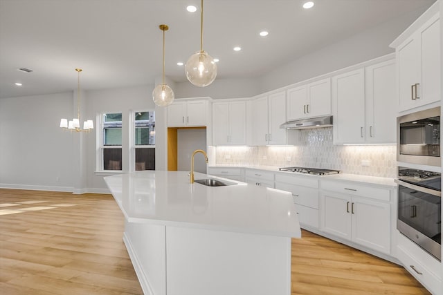 kitchen featuring pendant lighting, white cabinets, stainless steel appliances, sink, and a kitchen island with sink