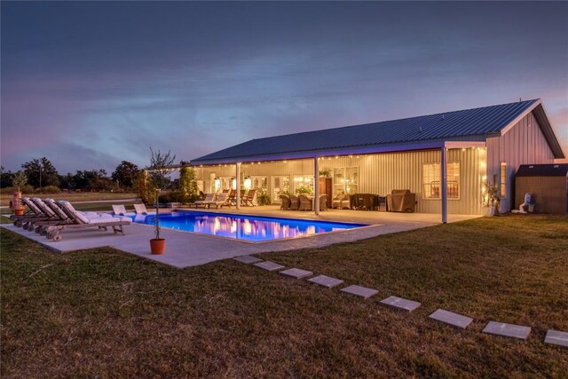 pool at dusk with a patio and a lawn