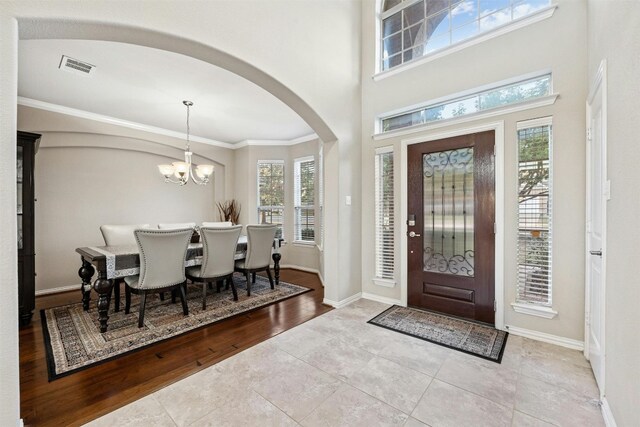 entrance foyer featuring light hardwood / wood-style flooring, ornamental molding, a wealth of natural light, and an inviting chandelier