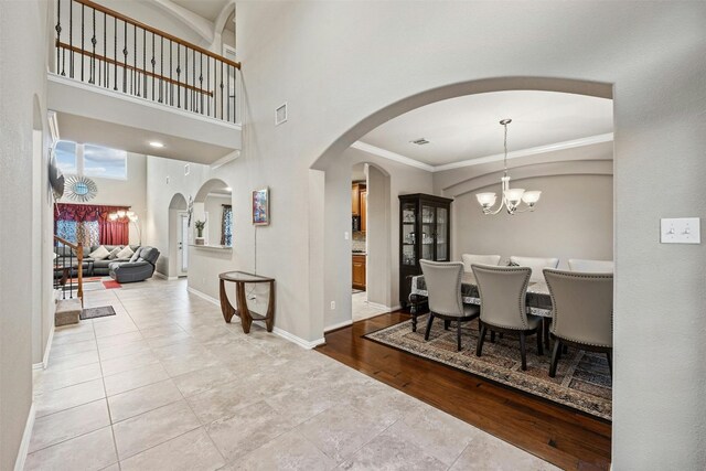 interior space featuring a towering ceiling, a notable chandelier, light wood-type flooring, and crown molding