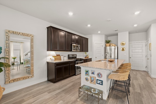 kitchen featuring stainless steel appliances, light hardwood / wood-style flooring, a kitchen bar, and a center island with sink