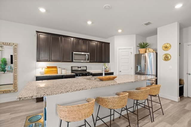 kitchen featuring a center island with sink, appliances with stainless steel finishes, a breakfast bar area, and light wood-type flooring