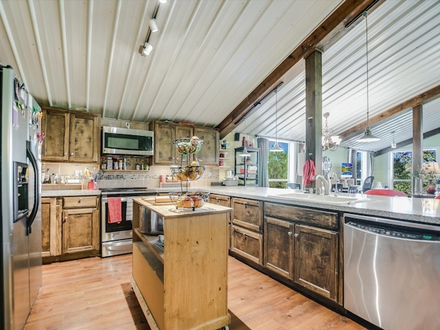 kitchen featuring appliances with stainless steel finishes, sink, light wood-type flooring, a center island, and hanging light fixtures