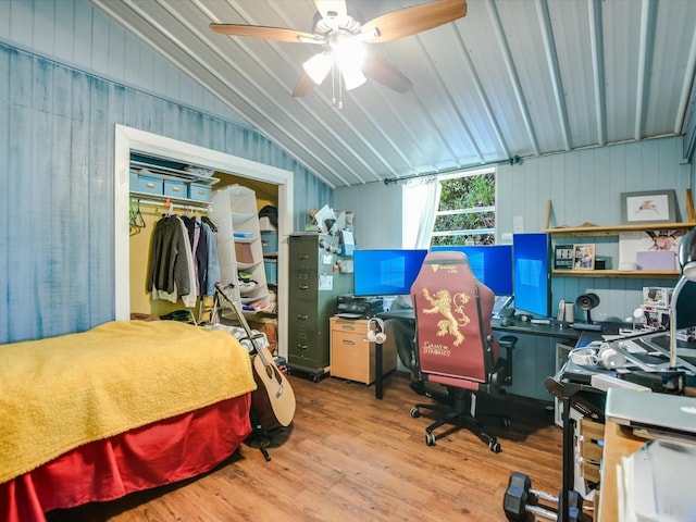 bedroom with light wood-type flooring, a closet, ceiling fan, vaulted ceiling, and wooden walls