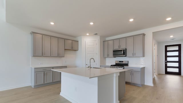 kitchen with appliances with stainless steel finishes, sink, an island with sink, light hardwood / wood-style floors, and gray cabinets